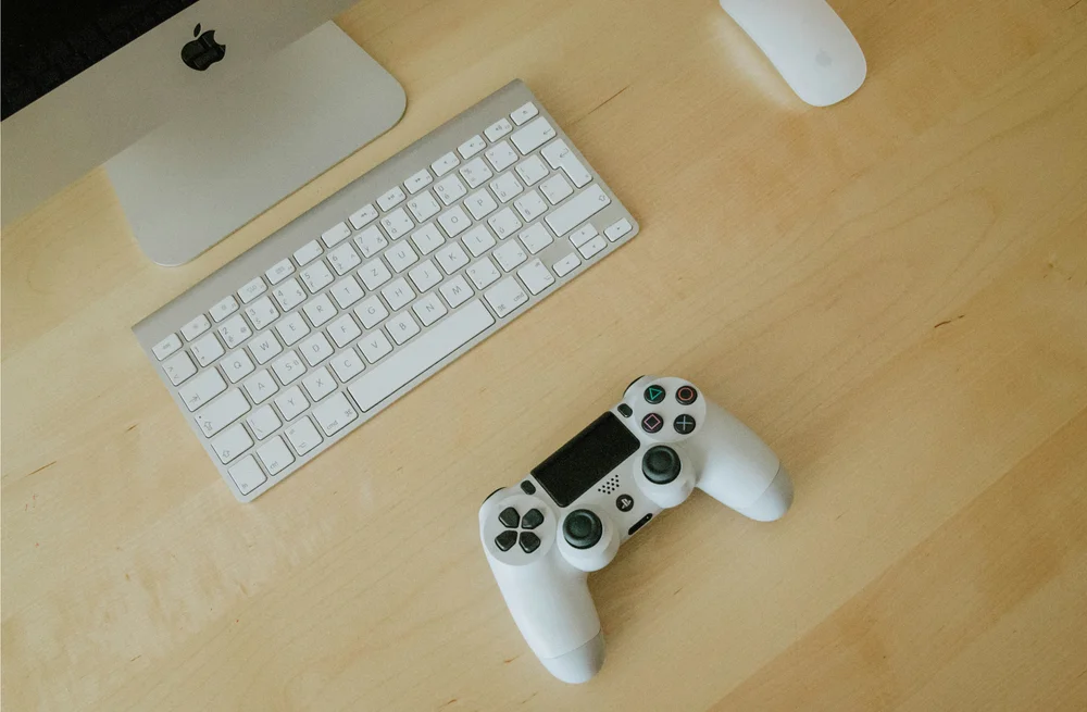 A white game controller beside a keyboard on a wooden desk