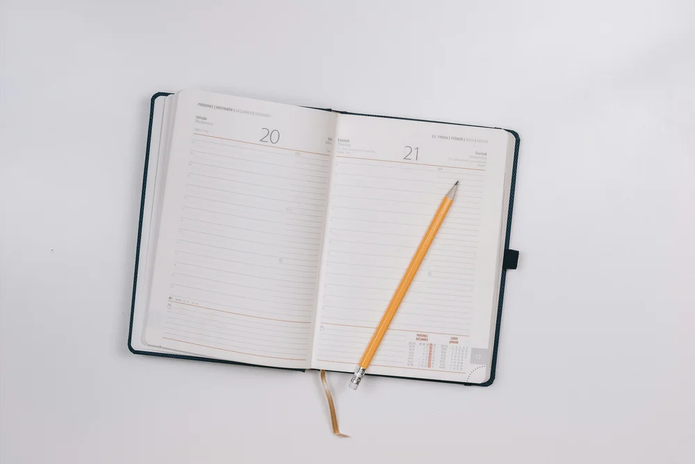 An open planner and a yellow pencil on a light desk