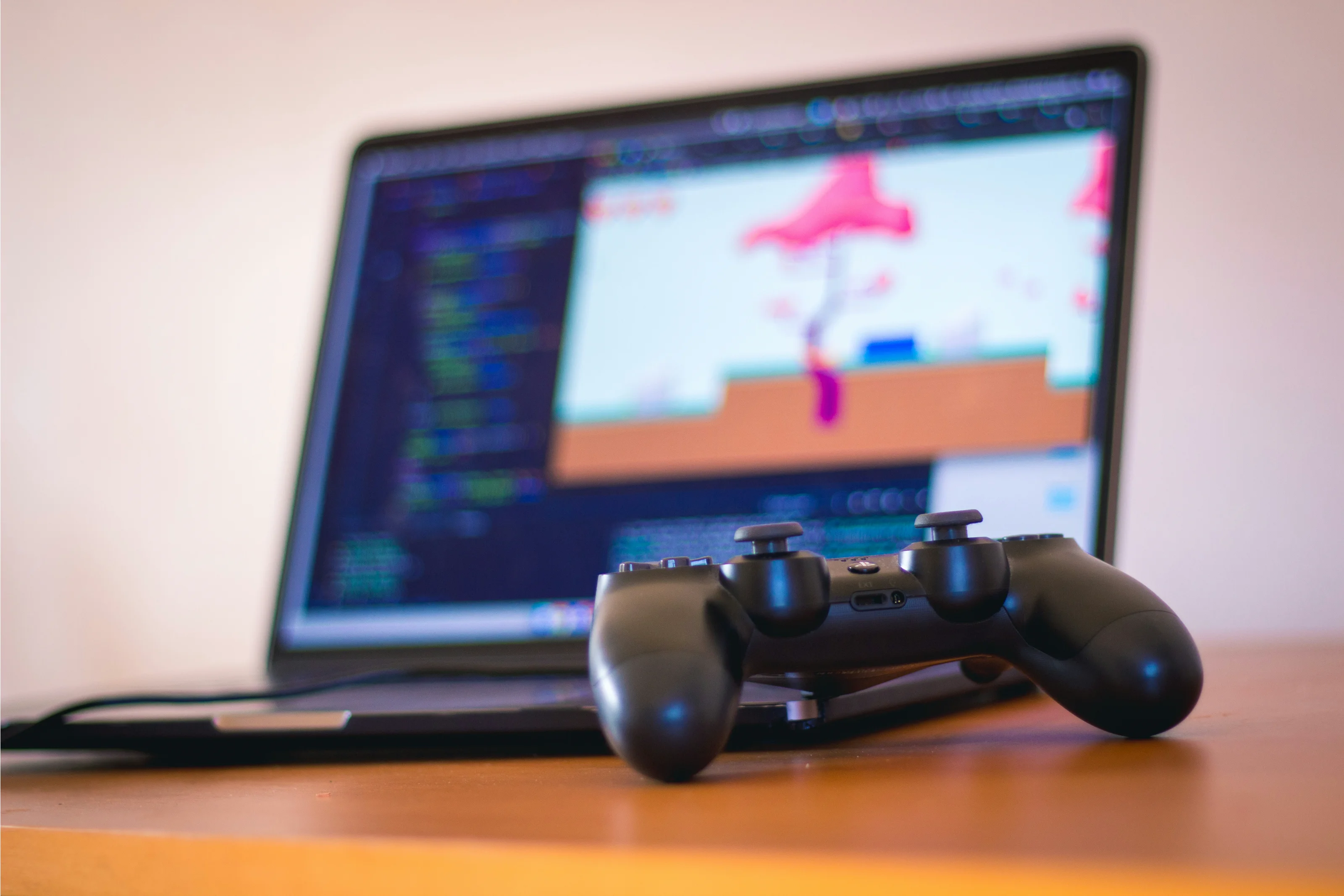 A black game controller in front of a laptop displaying a colourful game scene
